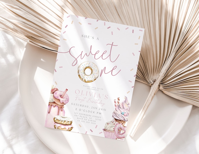 May include: A pink and white invitation card with a donut theme. The text reads "She's a Sweet One" and "Olivia's First Birthday". The invitation includes details for the event, including the date, time, and location.