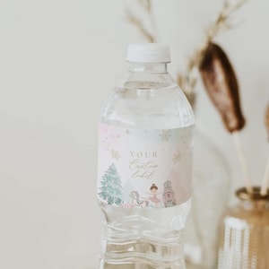 May include: A clear plastic water bottle with a white cap. The bottle has a custom label with a winter theme, featuring a Christmas tree, ballerina, and nutcracker in pastel colors. The label reads "Your Custom Label".
