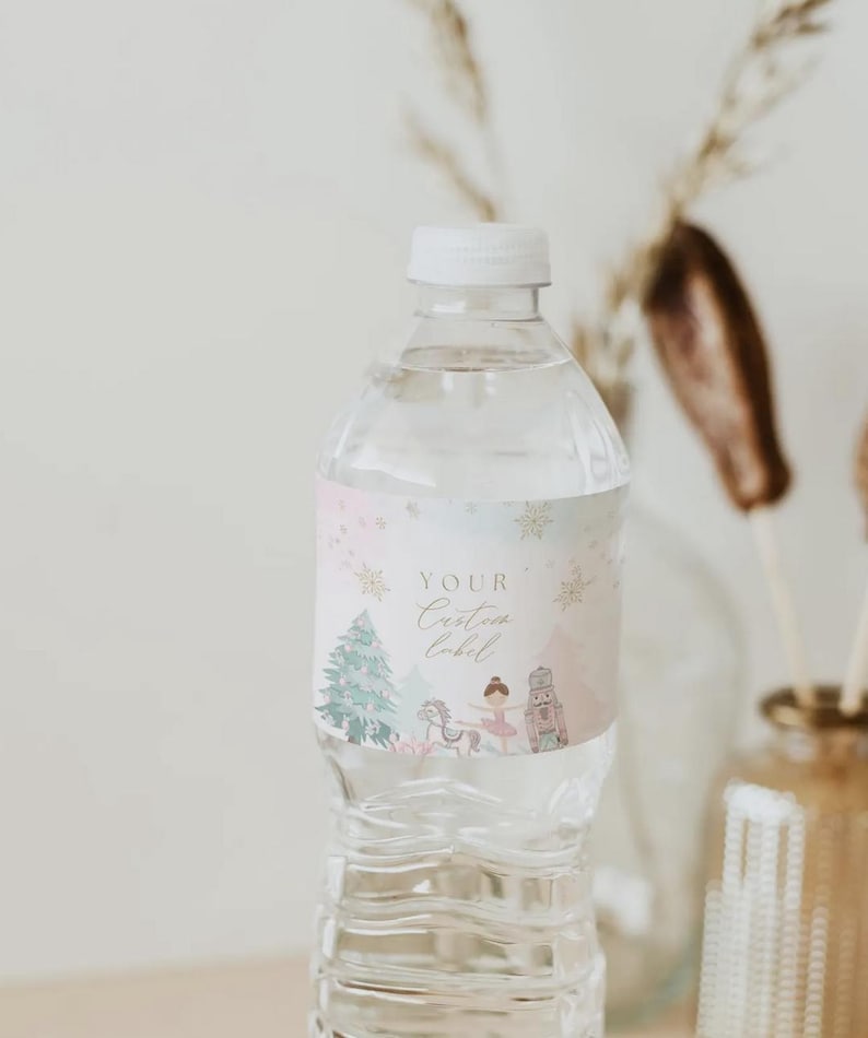 May include: A clear plastic water bottle with a white cap. The bottle has a custom label with a winter theme, featuring a Christmas tree, ballerina, and nutcracker in pastel colors. The label reads "Your Custom Label".