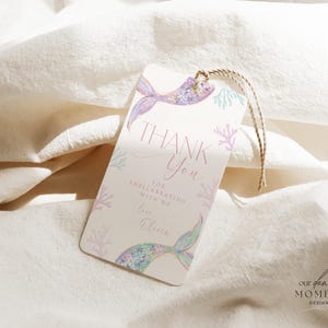 May include: A thank you tag with a mermaid tail design in shades of pink, purple, and blue. The tag says "Thank You" and "For celebrating with me Love, [Name]" with a coral and seaweed design.