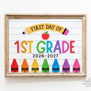 May include: A framed sign with a white background featuring blue horizontal lines like notebook paper. It displays the text FIRST DAY OF with a yellow pencil graphic, a red apple, the text 1ST GRADE in rainbow colours, and 2026-2027 below.