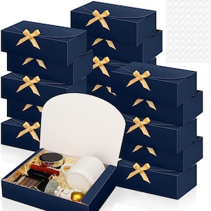 May include: A stack of 10 navy blue gift boxes with gold ribbon bows. The boxes are arranged in a pyramid shape. The top box is open and contains a white mug, a jar of lotion, a bar of soap, a small bottle of perfume, and a gold ornament.