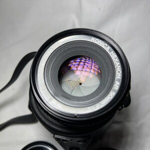 May include: A black Konica Hexanon AR 50mm f1.8 lens with a silver ring around the lens barrel. The lens is in focus and the aperture blades are visible.