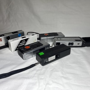 Può includere: Una collezione di fotocamere tascabili 110 vintage in vari colori, tra cui argento, nero e bianco. Alcune fotocamere hanno pulsanti rossi, blu e verdi. Una fotocamera ha la scritta "110 Pocket Camera".