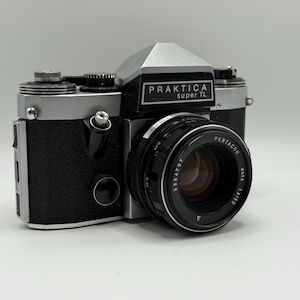 Peut inclure: Un appareil photo argentique 35 mm Praktica super TL avec un boîtier argenté et noir. L'appareil est équipé d'un objectif Pentacon auto 1.8/50, d'un prisme proéminent, d'une poignée noire texturée et de divers cadrans de réglage manuels.