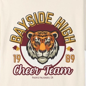 May include: A white t-shirt with a maroon and gold Bayside High cheer team logo. The logo features a tiger head with the text "Bayside High" in a gold circle and "Cheer Team" in maroon text below. The years 1989 are also included in the logo.