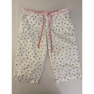 Puede incluir: Pantalones capri blancos con un pequeño estampado floral en azul y rojo. Los pantalones tienen una cintura elástica con un cordón rosa, dos bolsillos delanteros y cierre de botones. La tela es ligera con un diseño de dobladillo vuelto.