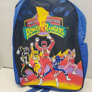 Könnte beinhalten: Blauer Rucksack mit schwarzem Hintergrund, auf dem das Mighty Morphin Power Rangers Logo und die fünf Power Rangers in ihren ikonischen Posen abgebildet sind. Der Text "Mighty Morphin Power Rangers" ist in Weiß mit einem gelben Blitz gedruckt.