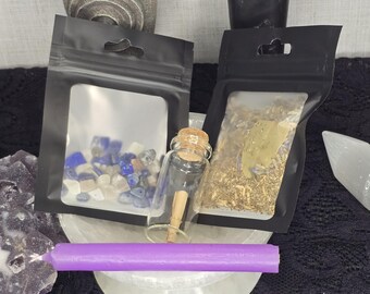May include: A collection of spiritual items, including a small glass bottle with a cork, two black pouches with clear windows, and a long, purple candle. The pouches contain small stones and dried herbs. The items are arranged on a white, circular stand.