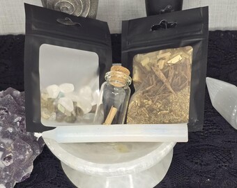 May include: Two black zippered pouches, one containing clear crystals and the other containing dried herbs, a small glass bottle with a cork stopper, and a white, round, smooth stone.