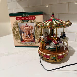 May include: A Mr. Christmas HolidayGoRound collectible carousel featuring a striped canopy in red, white, and green with gold accents. The base is red with gold detailing, and the carousel includes several painted figures riding horses.