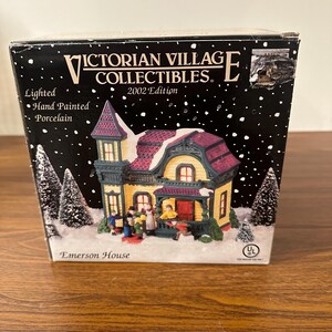 May include: A lighted porcelain Victorian Village Collectibles Emerson House, hand-painted in yellow, green, and purple with a red roof. The house has a porch with a white railing and a red door. There are miniature figures of people in front of the house. The box is labeled "Victorian Village Collectibles 2002 Edition" and "Emerson House".