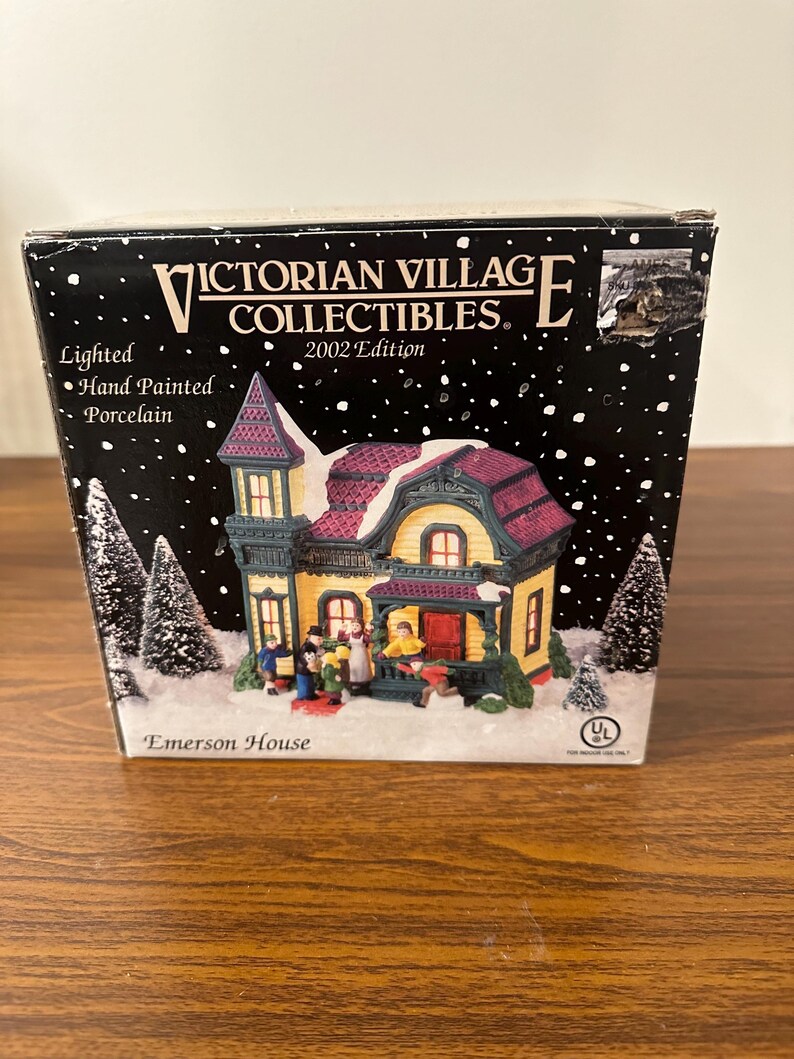 May include: A lighted porcelain Victorian Village Collectibles Emerson House, hand-painted in yellow, green, and purple with a red roof. The house has a porch with a white railing and a red door. There are miniature figures of people in front of the house. The box is labeled "Victorian Village Collectibles 2002 Edition" and "Emerson House".