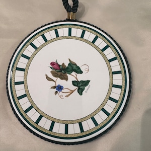 May include: Round ceramic hot pad with a green and white striped border. The center features a floral design with a pink rose, green leaves, and a blue flower. The text "LENOX" is printed on the pad.