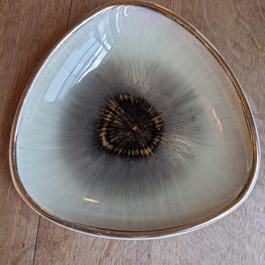 May include: A triangular ceramic serving dish with a white and gray glaze. The center of the dish has a black and gold design.