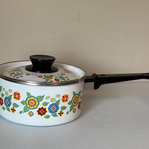 Peut inclure: Casserole en émail blanc avec une poignée et un couvercle noirs. Le pot est décoré d'un motif floral rouge, bleu, jaune et vert. Un article de cuisine vintage.