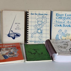 Może przedstawiać: Kolekcja starych książek kucharskich ze spiralnymi oprawami. Tytuły to "Recipes", "Music in your Menus", "Eat Yer Heart Oot", "River East Collegiate Musical Arts Cook Book" i "Sugar and Spice and Everything NICU."