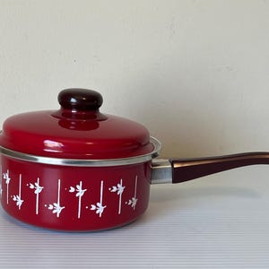 May include: Red enamel saucepan with a white floral design and a brown handle.