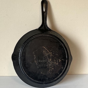 May include: A black cast iron skillet with a long handle and a round cooking surface. The bottom of the skillet has the text "JAPAN" and other markings. The skillet is designed for cooking.