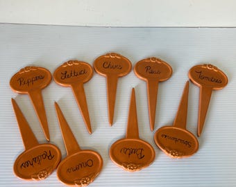 May include: Set of ten orange plastic garden plant markers with black lettering. The markers are labeled with the names of different vegetables and herbs, including: Peppers, Lettuce, Chives, Peas, Tomatoes, Radishes, Onions, Dill, and Spinach.
