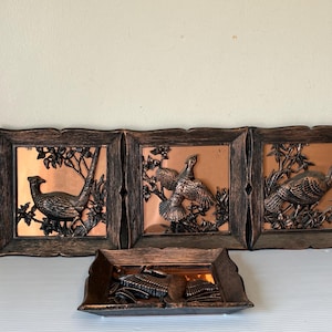 May include: Set of three framed copper-colored wall art pieces, each featuring a detailed relief of a pheasant in a natural setting. The frames are dark brown with a rustic finish. A matching copper-toned tray is below.