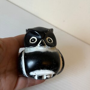 May include: Black and white ceramic owl figurine with large eyes. The owl is sitting on a hand.