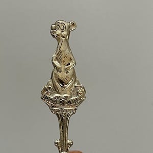 Peut inclure: Cuillère souvenir en argent avec une figurine de kangourou sur le dessus. La cuillère porte l'inscription "Australie" gravée sur le manche.