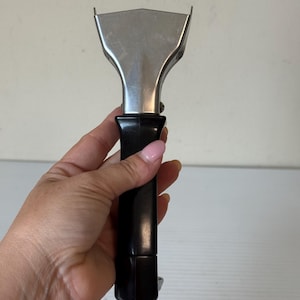 May include: A stainless steel grill scraper with a black handle. The scraper has a flat, angled blade for cleaning grill surfaces. The handle is made of a smooth, black material, providing a comfortable grip. The tool is designed for removing food residue.