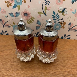 Puede incluir: Un juego de dos saleros y pimenteros vintage de vidrio con una base transparente en forma de diamante y un cuerpo octogonal rosa. Las tapas son plateadas con una tapa de rosca.