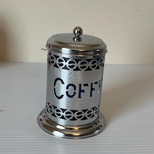 Peut inclure: Une boîte à café en argent avec un insert en verre bleu et un motif métallique décoratif. La boîte a un couvercle et indique "COFFEE" sur le devant.