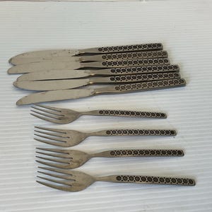 May include: A set of stainless steel flatware, including knives and forks. The knives have a smooth blade and a decorative handle with a repeating floral pattern. The forks also have the same patterned handles.