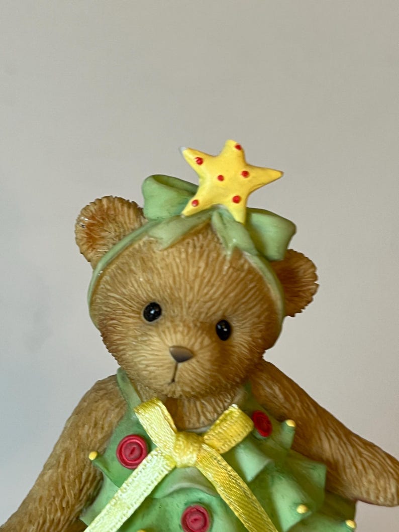 Puede incluir: Un oso de peluche marr&oacute;n vestido como un &aacute;rbol de Navidad. El oso lleva un vestido verde con una cinta amarilla y botones rojos. El oso tiene una estrella amarilla en la cabeza.