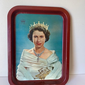 Op de afbeelding: Een rood metalen dienblad met een afbeelding van koningin Elizabeth II die een kroon en een witte jurk draagt. Het dienblad heeft een koninklijk wapen met de letters "E.R." in de linkerbovenhoek.