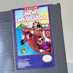 May include: A Nintendo Entertainment System game cartridge for Mickey Mousecapade. The label features Mickey Mouse, Goofy, and other characters on a ship. The cartridge is gray with the name "JONATHAN" printed on it.