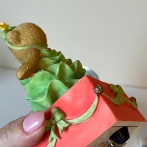 Puede incluir: Una figurita musical de &aacute;rbol de Navidad con un oso marr&oacute;n vestido como &aacute;rbol de Navidad. La figurita est&aacute; en una caja roja con una cinta verde y una campana dorada.