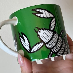 May include: A green ceramic mug with a white handle and a black and white illustration of a scorpion on the front.