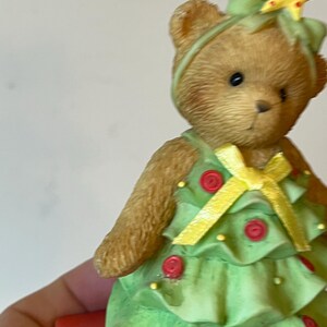 Puede incluir: Un oso de peluche marr&oacute;n vestido como un &aacute;rbol de Navidad. El oso lleva un vestido verde con botones rojos y una cinta amarilla. El oso tiene una estrella amarilla en la cabeza.