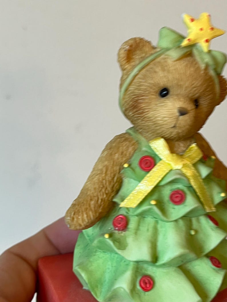 Puede incluir: Un oso de peluche marr&oacute;n vestido como un &aacute;rbol de Navidad. El oso lleva un vestido verde con botones rojos y una cinta amarilla. El oso tiene una estrella amarilla en la cabeza.