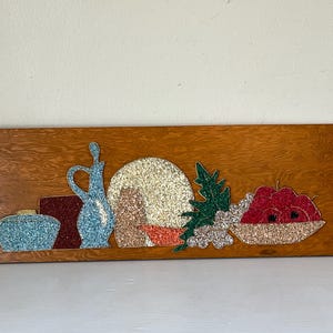 May include: A vintage wooden wall art piece with a still life design. The artwork includes a blue jug, a red block, a bowl of red apples, and other decorative elements, all with a textured, glittery finish.