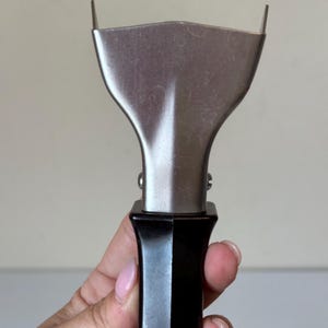 May include: A stainless steel spatula with a black handle. The spatula has a wide, flat blade with two small, raised edges. The handle is a glossy black, and the spatula appears to be new.