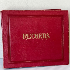 Puede incluir: Un libro encuadernado en cuero rojo con letras doradas que dicen "RECORDS".