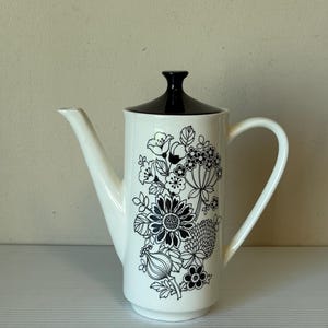 Puede incluir: Cafetera de cerámica blanca con tapa y asa negras. La cafetera está decorada con un estampado floral negro. El pico es largo y delgado, y el asa es curva. Diseño clásico.