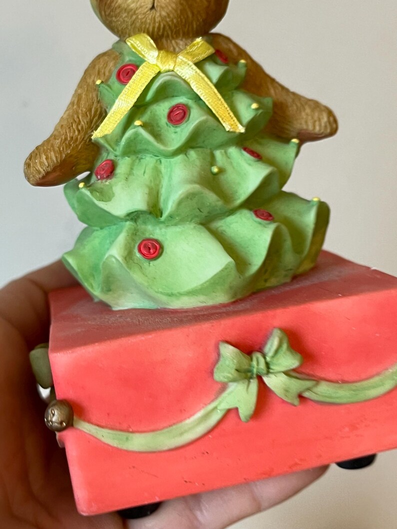 Puede incluir: Un oso de peluche marr&oacute;n vestido como un &aacute;rbol de Navidad con un lazo amarillo y adornos rojos. El oso est&aacute; de pie sobre una caja roja con un lazo verde.