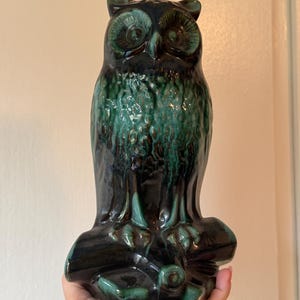 May include: A ceramic owl figurine featuring a glossy glaze in shades of deep black and vibrant emerald green. The owl is depicted perched on a branch with detailed feather textures, large circular eyes, and pointed ear tufts in a dark finish.