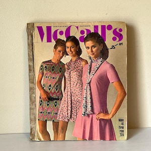 May include: Vintage McCall's sewing pattern book featuring three women modeling dresses. The cover has the title "McCall's" in large purple letters, with the month "April" visible. The cover shows the models wearing dresses in pink, green, and patterned fabrics.