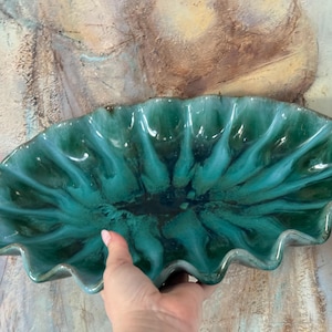 May include: A teal ceramic serving dish with a ruffled edge. The dish has a glossy finish and a dark centre, with a rippled design. The dish is held in a hand.