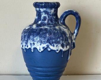 May include: A blue ceramic pitcher with a handle. The top portion is speckled with white, creating a drip effect over the solid blue base. The pitcher has a rounded body with horizontal ridges.