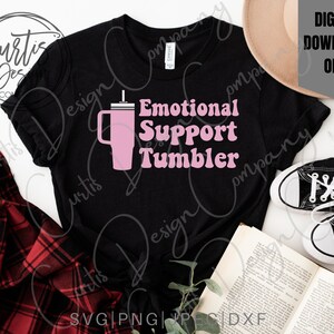 May include: A black t-shirt with a pink graphic of a tumbler with a straw and the text "Emotional Support Tumbler" in a retro font.