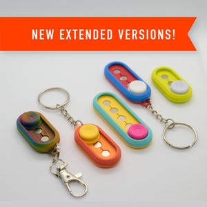 May include: Four colorful keychains with different designs. Each keychain features a round button that can be pressed and spun. The keychains are made of plastic and have a silver metal ring.