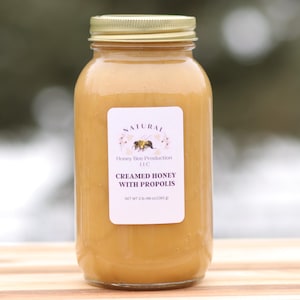 May include: A jar of creamed honey with propolis. The honey is a light amber color and has a smooth, creamy texture. The jar has a gold lid and a white label with the words "Creamed Honey with Propolis". The jar contains 2.19 oz (62 g) of honey.